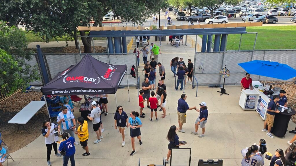 Fans entering Nelson Wolff Stadium at the home plate entrance. Two booths with vendors on each side with fans entering through the middle.